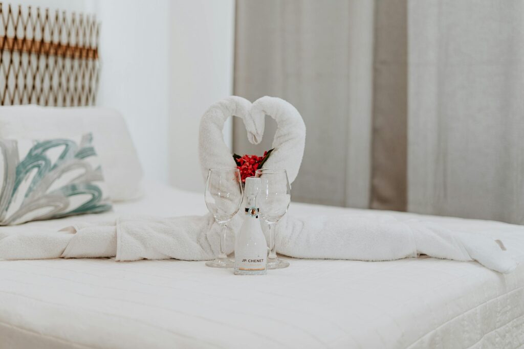 A luxurious hotel room with swan towel decoration and wine glasses on the bed.